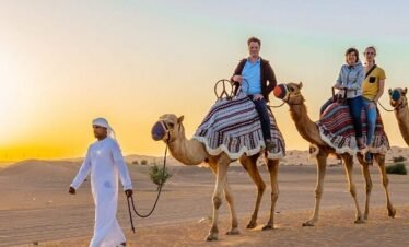 Tourist riding camel through dunes under guider